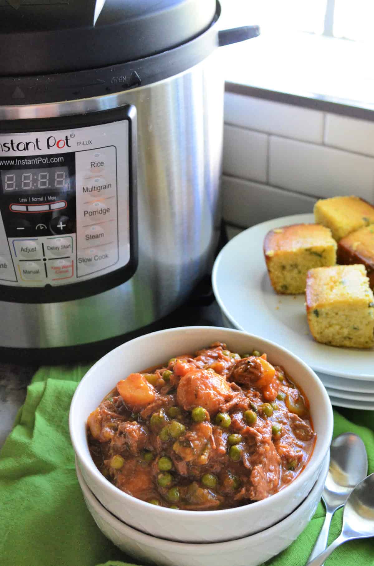 Closeup bowl beef stew on green cloth with corn bread and Instant Pot behind it.