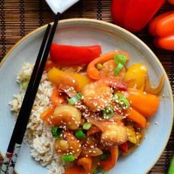 top view of bell peppers, shrimp, green onions topped with sesame seeds plated on bed of rice with chopsticks.