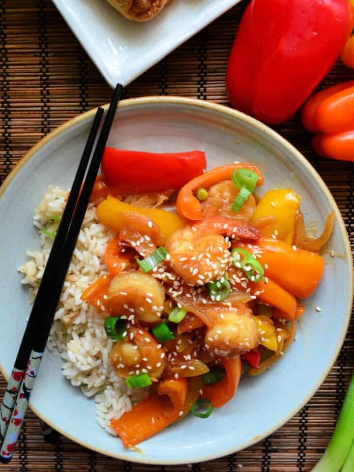 top view of bell peppers, shrimp, green onions topped with sesame seeds plated on bed of rice with chopsticks.