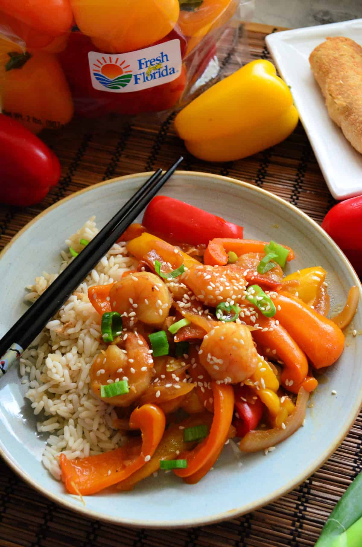 sauce, shrimp, peppers, green onions, and sesame seeds over plated rice bed with chopsticks.