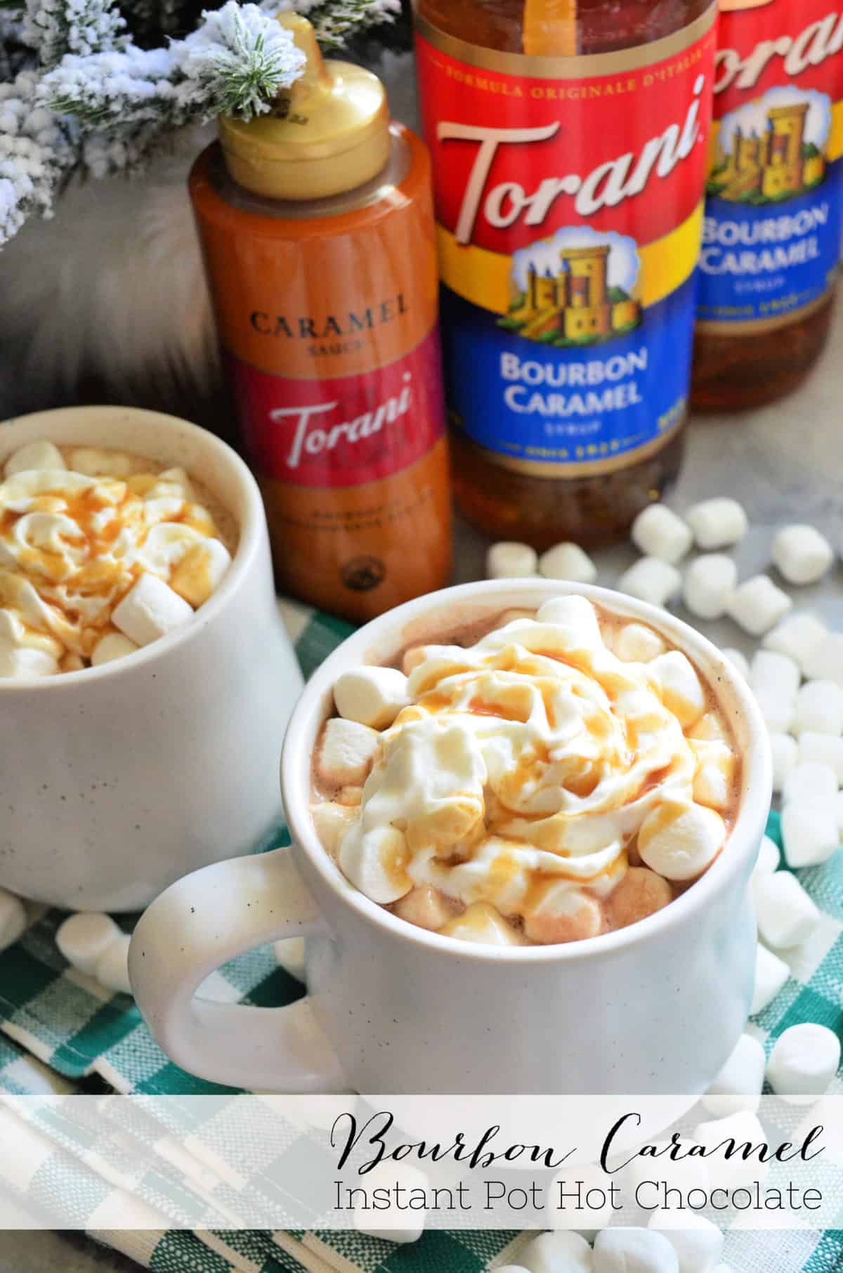 two mugs of brown liquid topped with mini marshmallows, whipped cream, and caramel with title text.