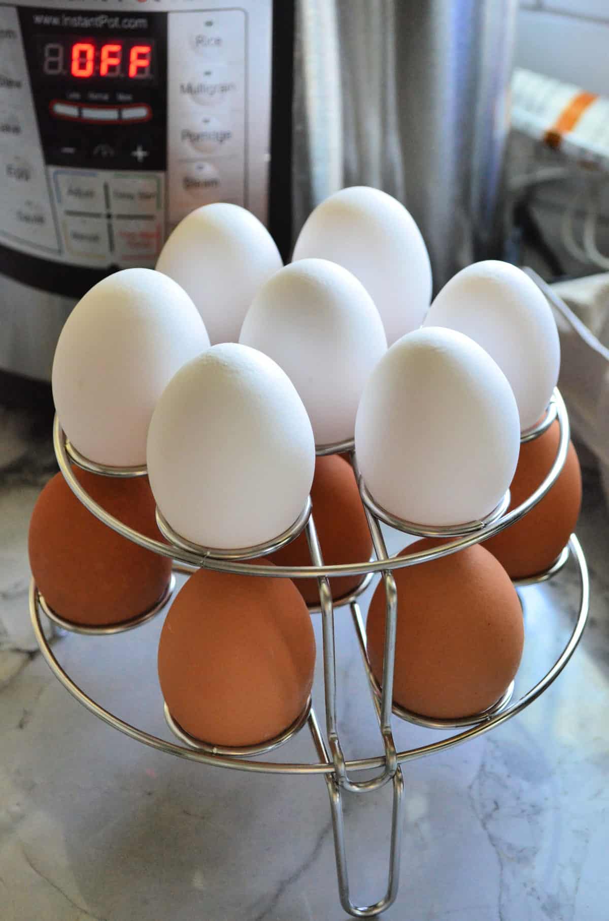 14 eggs resting on 2-level wire egg rack in front of instant pot.