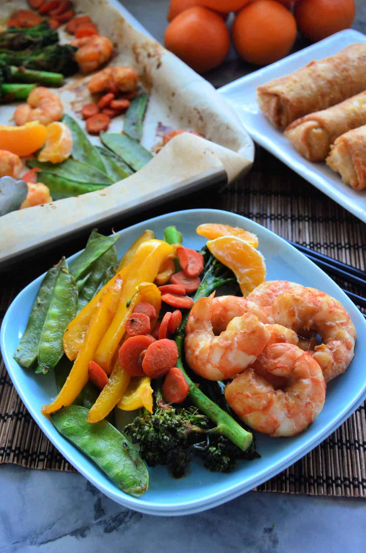 plated peas, broccolini, manadrine oranges, shrimp, bell pepper, and carrots with baking sheet in background.