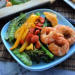 Square plate with shrimp, broccoli, bell peppers, carrots, and peas.