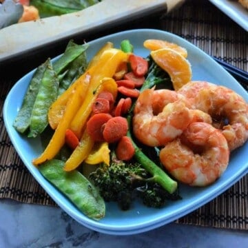 Square plate with shrimp, broccoli, bell peppers, carrots, and peas.