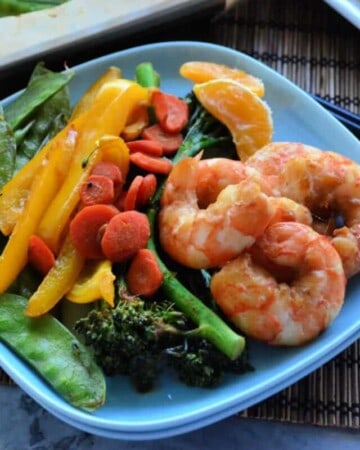 Square plate with shrimp, broccoli, bell peppers, carrots, and peas.