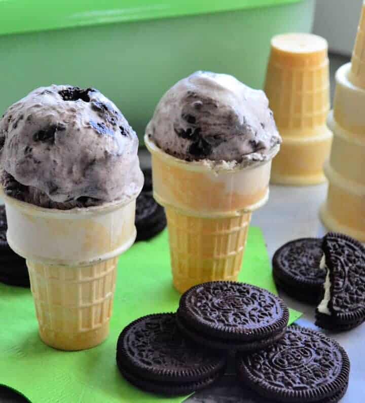 2 cones with one scoop each of cookies and cream ice cream on napkin next more cones.