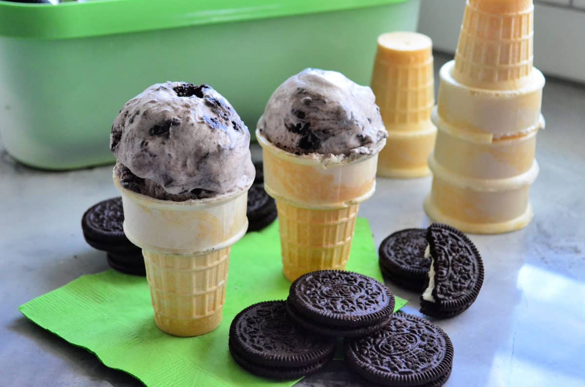 OREO cookies stacked in front of two cake cones filled with oreo ice cream. 