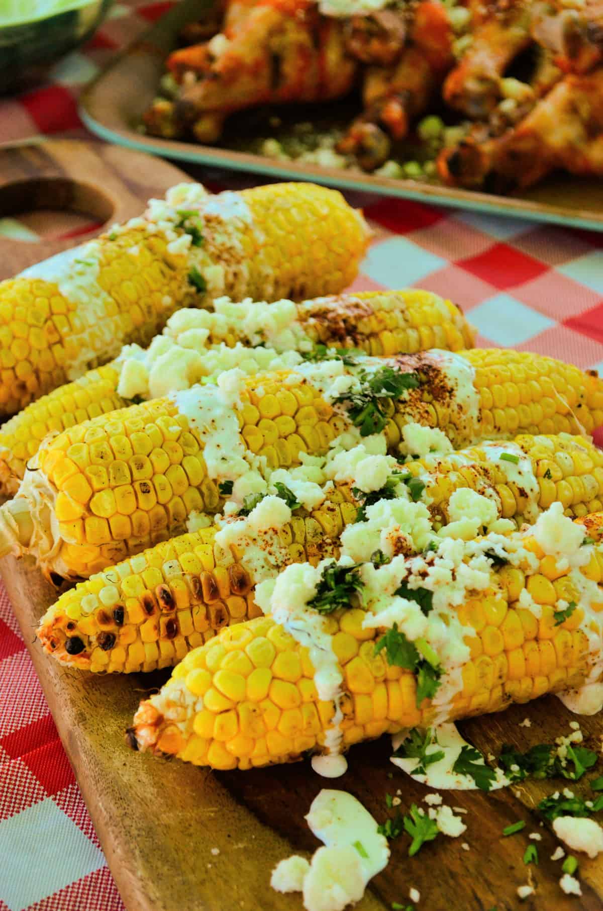 corn cobs on a board drizzled with crema, cheese crumbles, red powder, and herbs.