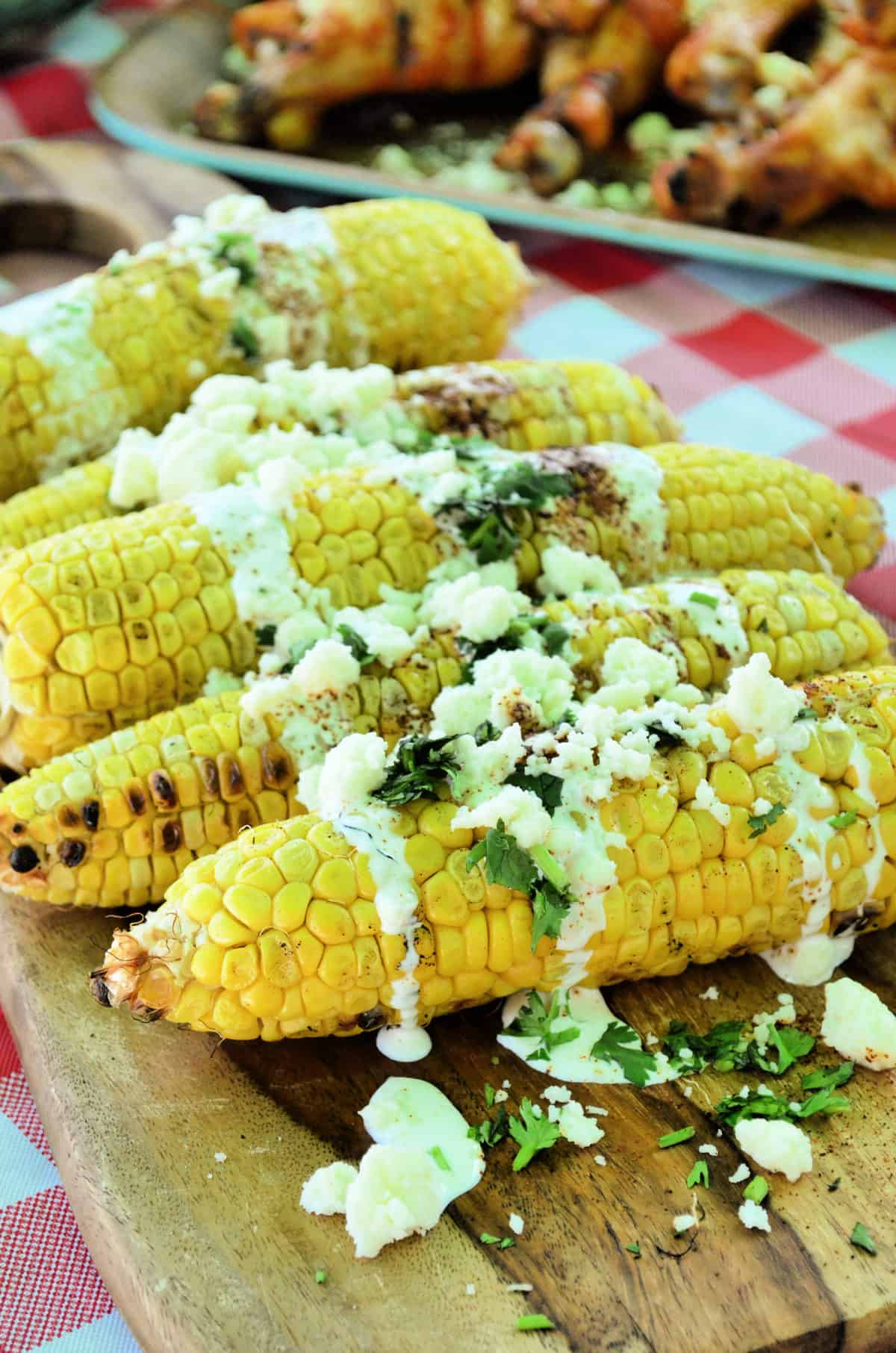 corn cobs on a board drizzled with crema, cheese crumbles, red powder, and herbs.