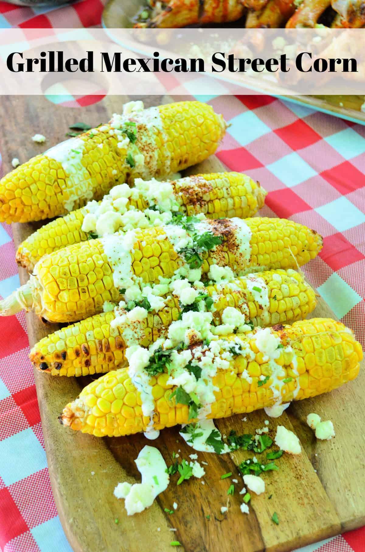 corn cobs on a board drizzled with crema, cheese crumbles, and herbs with title text.