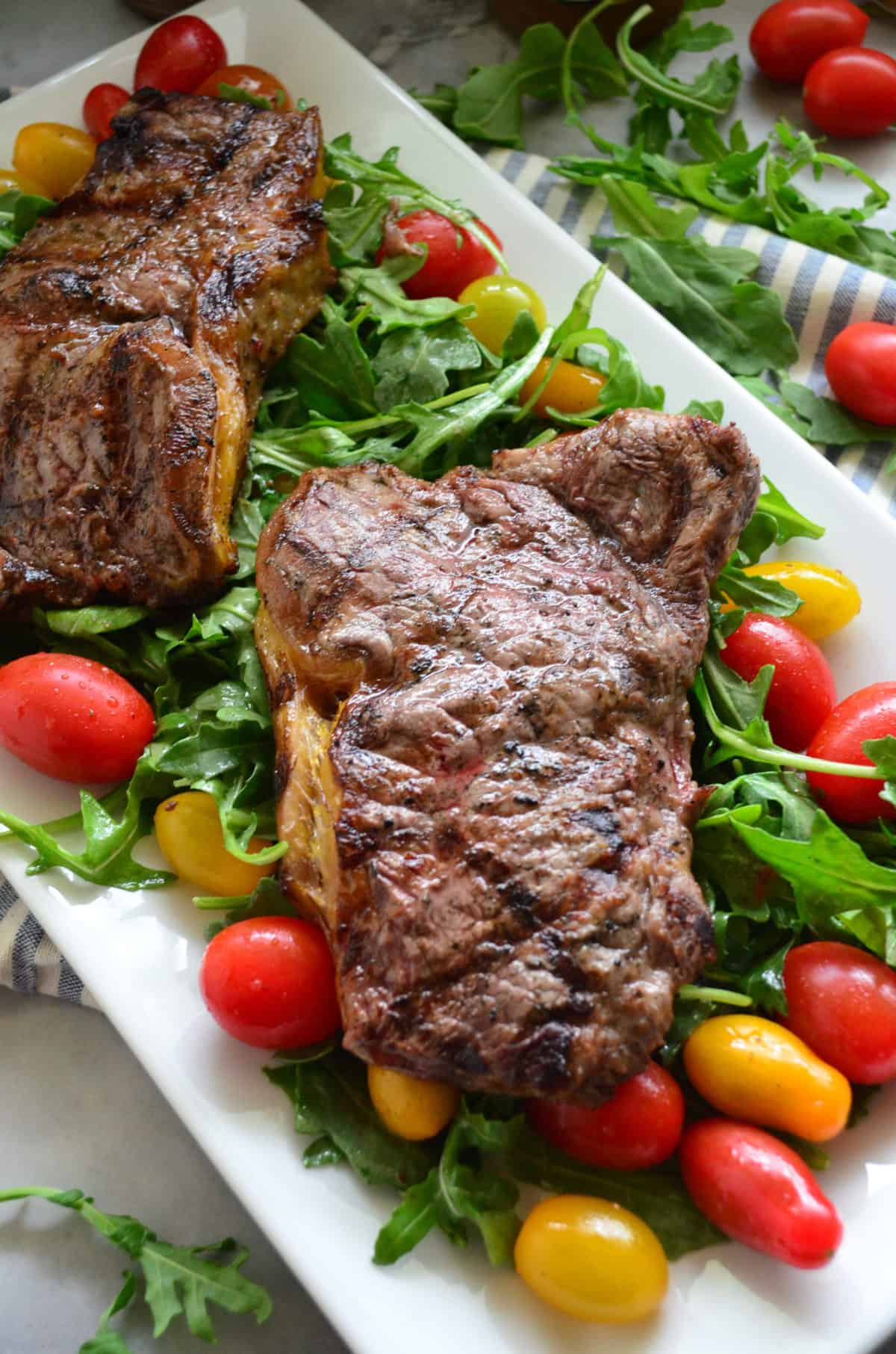 Close-up top view of 2 steaks on bed of arugula and tomato salad.