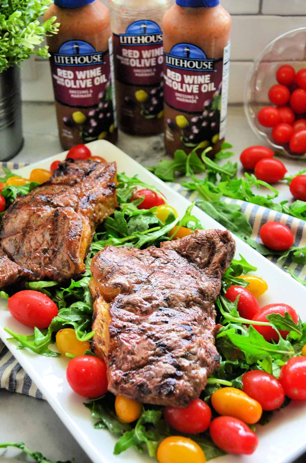 2 cooked steaks over bed of arugula salad with grape tomatoes with red wine olive oil dressing in background.