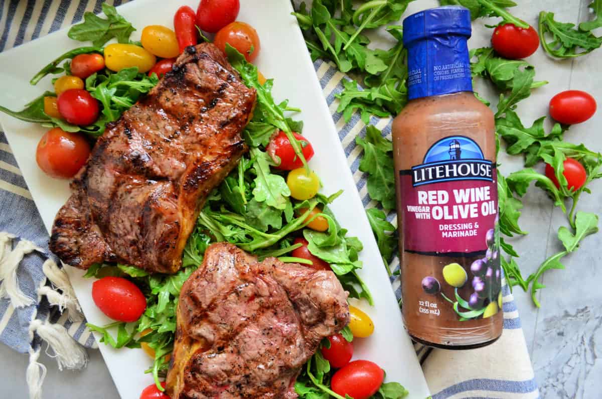 2 cooked steaks over bed of arugula salad with grape tomatoes with red wine olive oil dressing bottle.