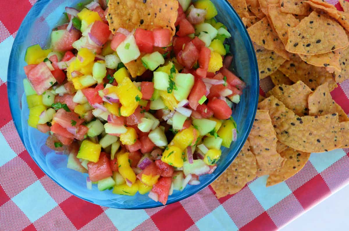 watermelon salsa with red onions, mangos, watermelon and green herbs most visible and served with chips.