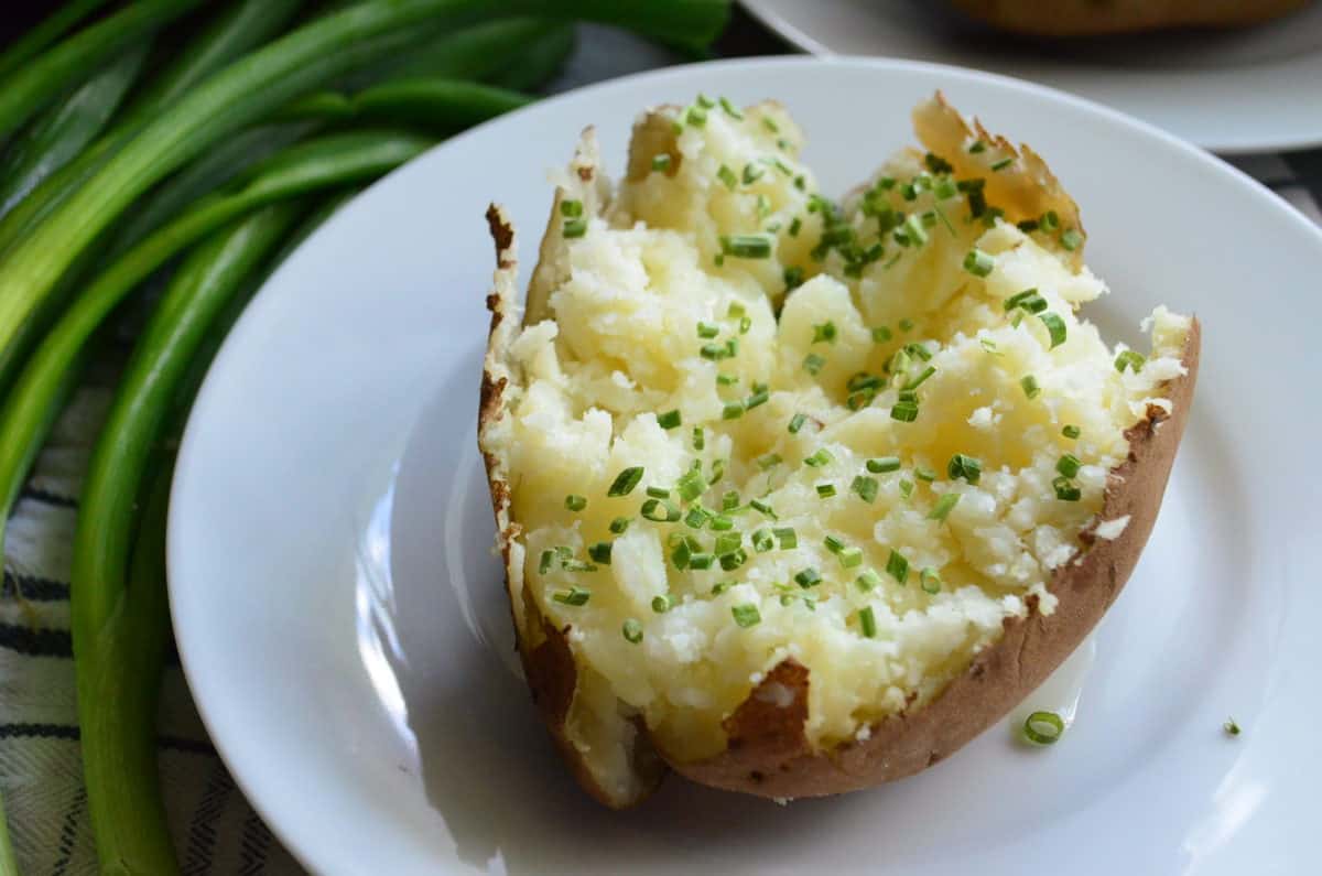 close up plated baked potato topped with chives next to whole chives.