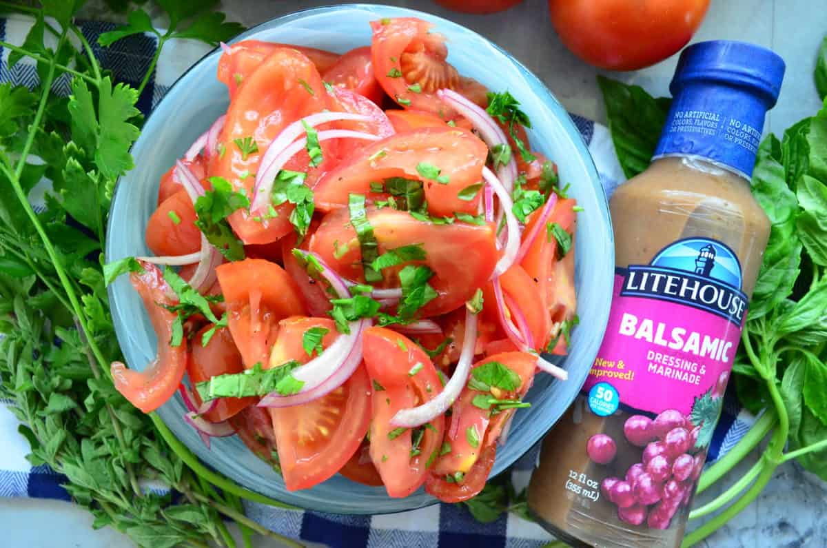 sliced tomatoes, red onion, basil, and dressing in bowl next to bottle of Litehouse Balsamic Dressing.