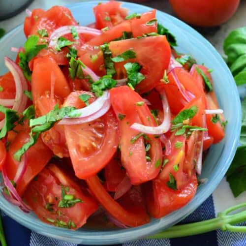 Blue bowl filled with tomatoes, red onions, and herbs.