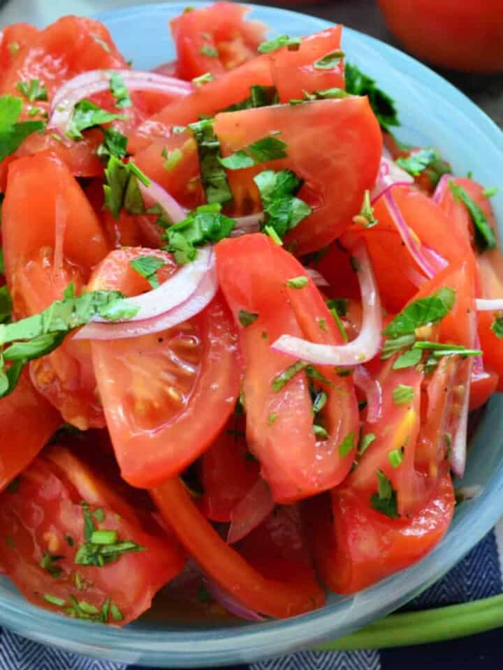 Blue bowl filled with tomatoes, red onions, and herbs.