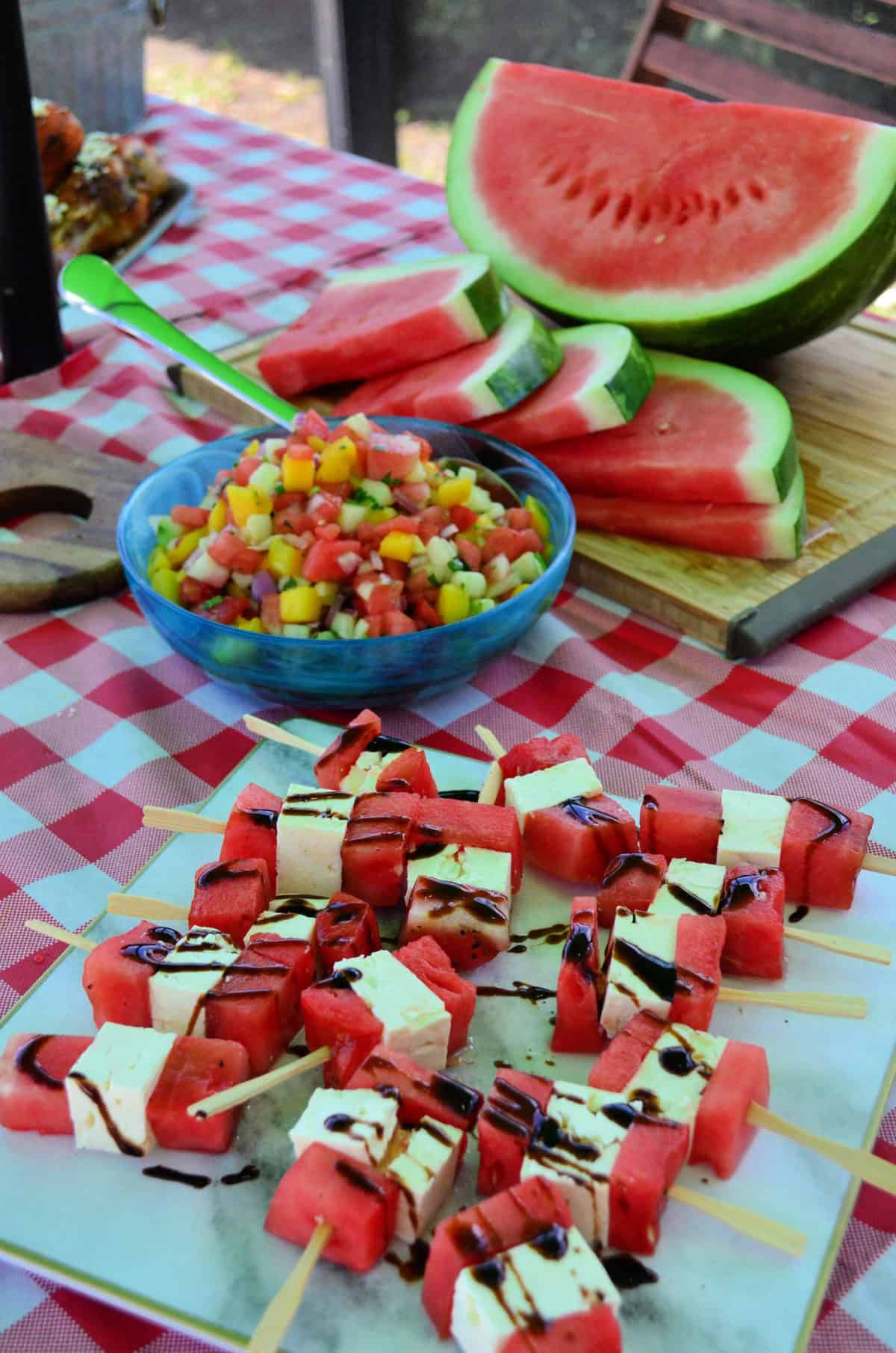 sliced watermelon on cutting board next to watermelon salsa and watermelon feta skewers.