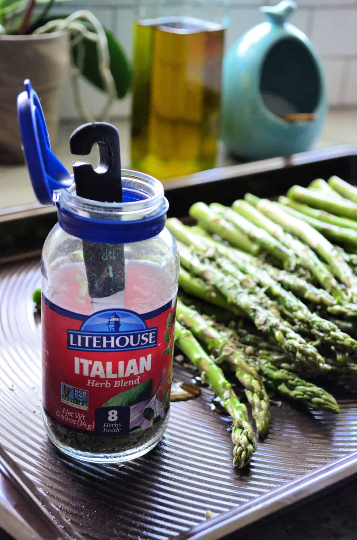 Close up of 1 teaspoon dipped into bottle of Litehouse Italian Herb blend set on asparagus pan.