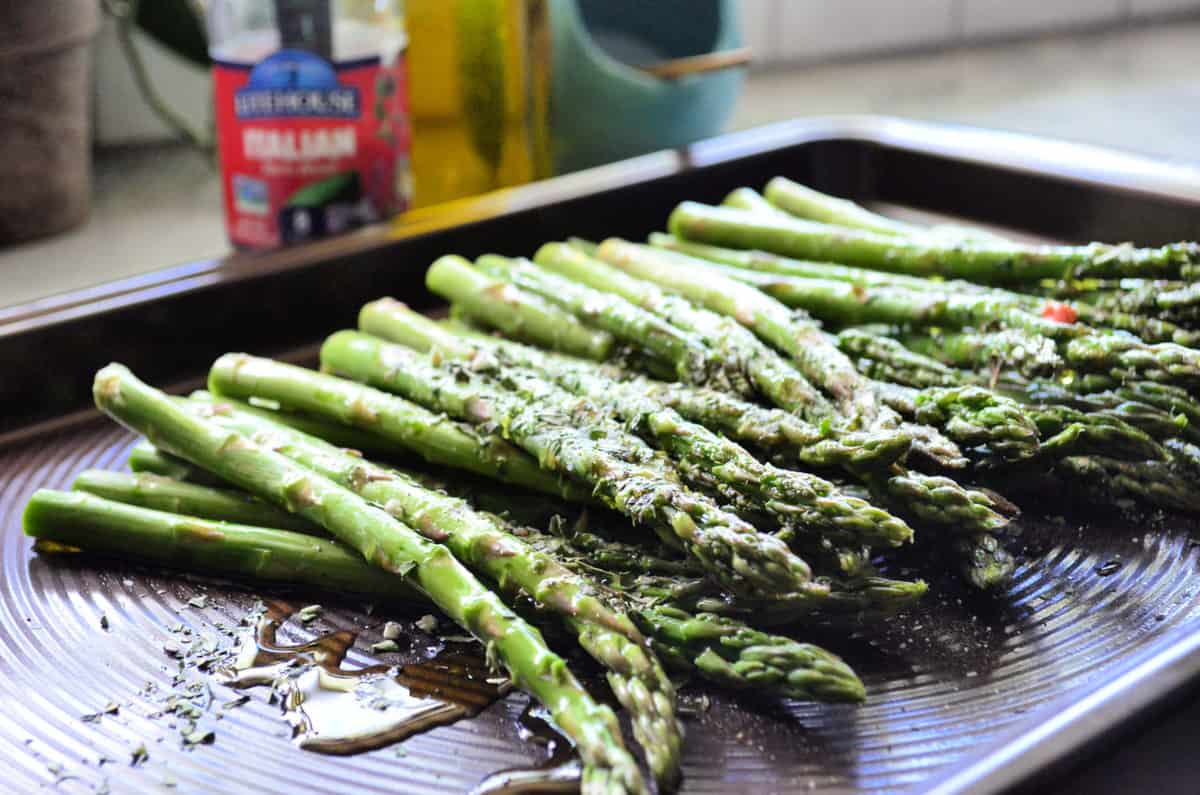 Baking pan full of asparagus glistening with oil in the light.