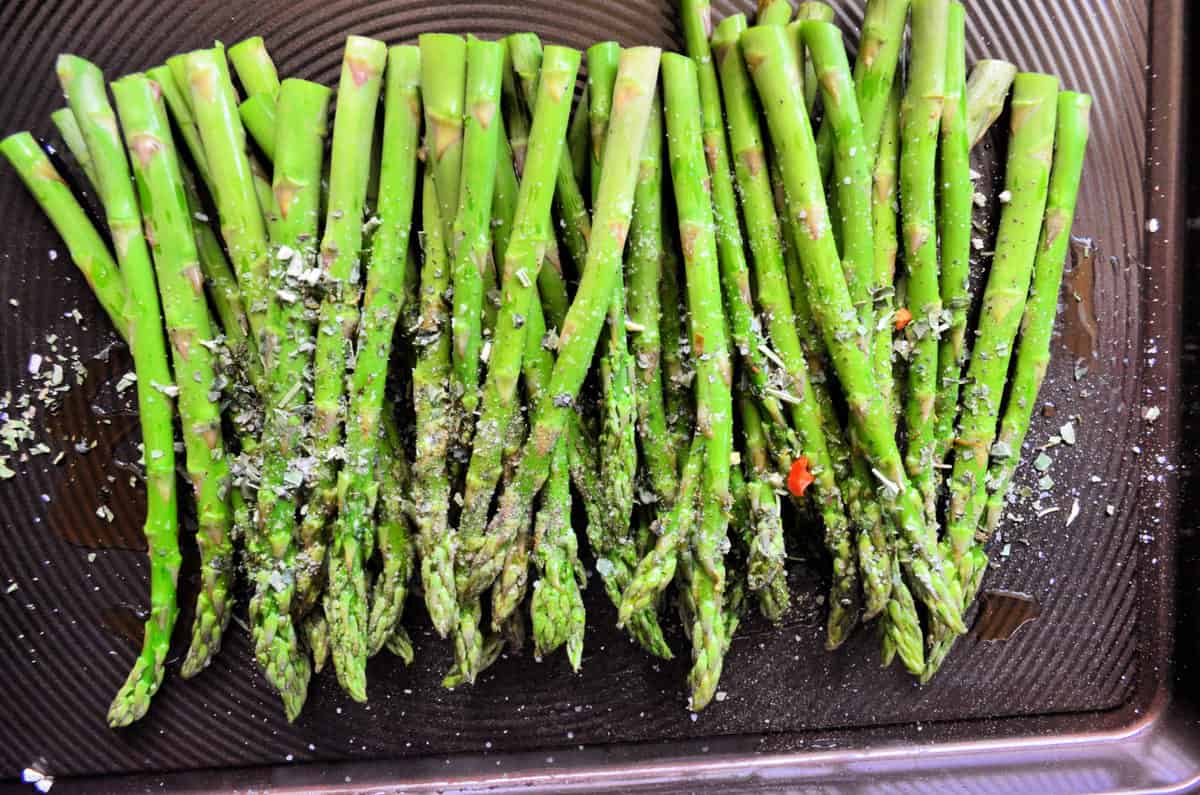 top view of grilled Italian Herb Asparagus on baking pan topped with herbs and cheese.