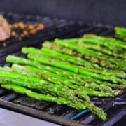 Side view of Italian Herb Asparagus on grill with meat blurred in background.