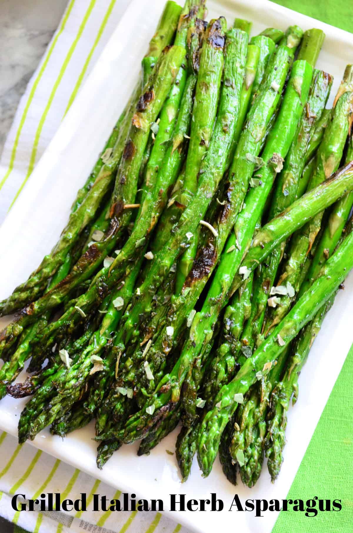 Closeup of grilled asparagus on rectangular platter with Italian herbs sprinkled on top and title text.