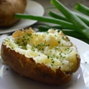 side view plated halved baked potato mashed on the inside with melted butter and chives.