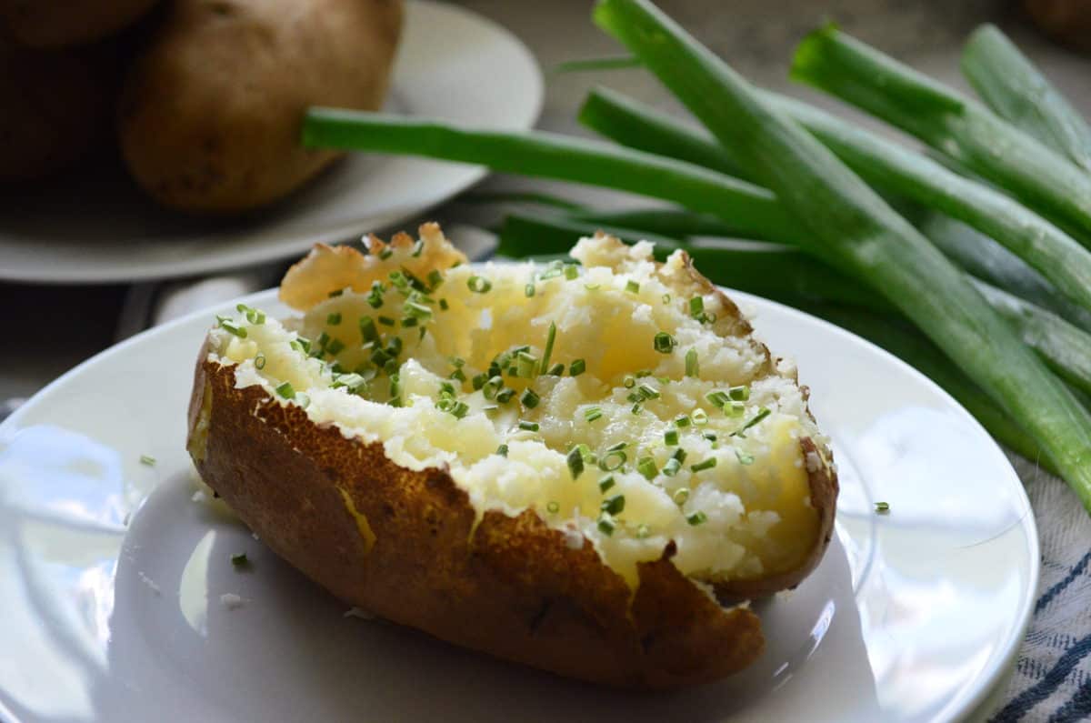 side view plated halved baked potato mashed on the inside with melted butter and chives.