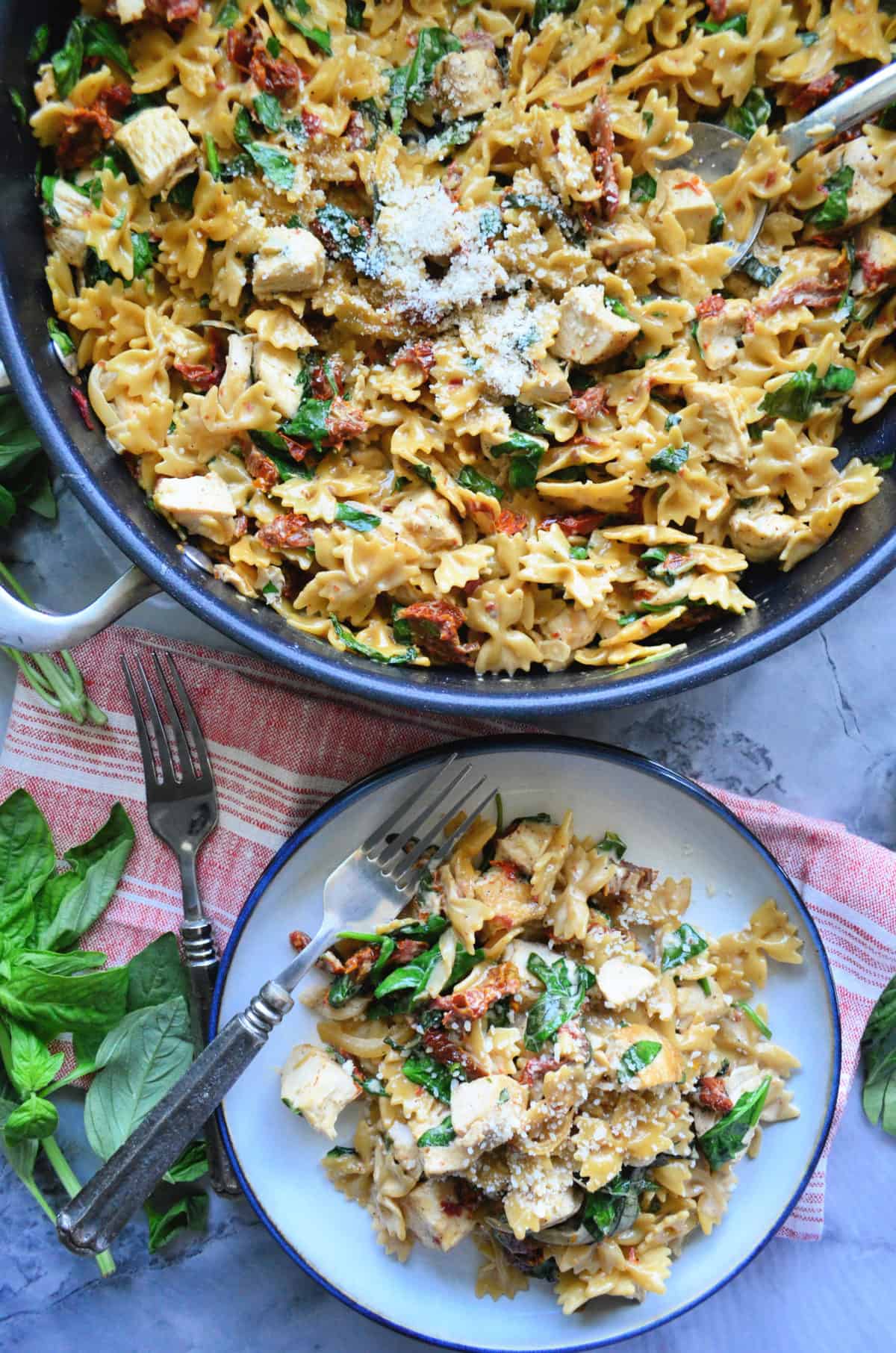 bowtie pasta, basil, sundried tomato chicken, and parmesan in skillet and on plate.