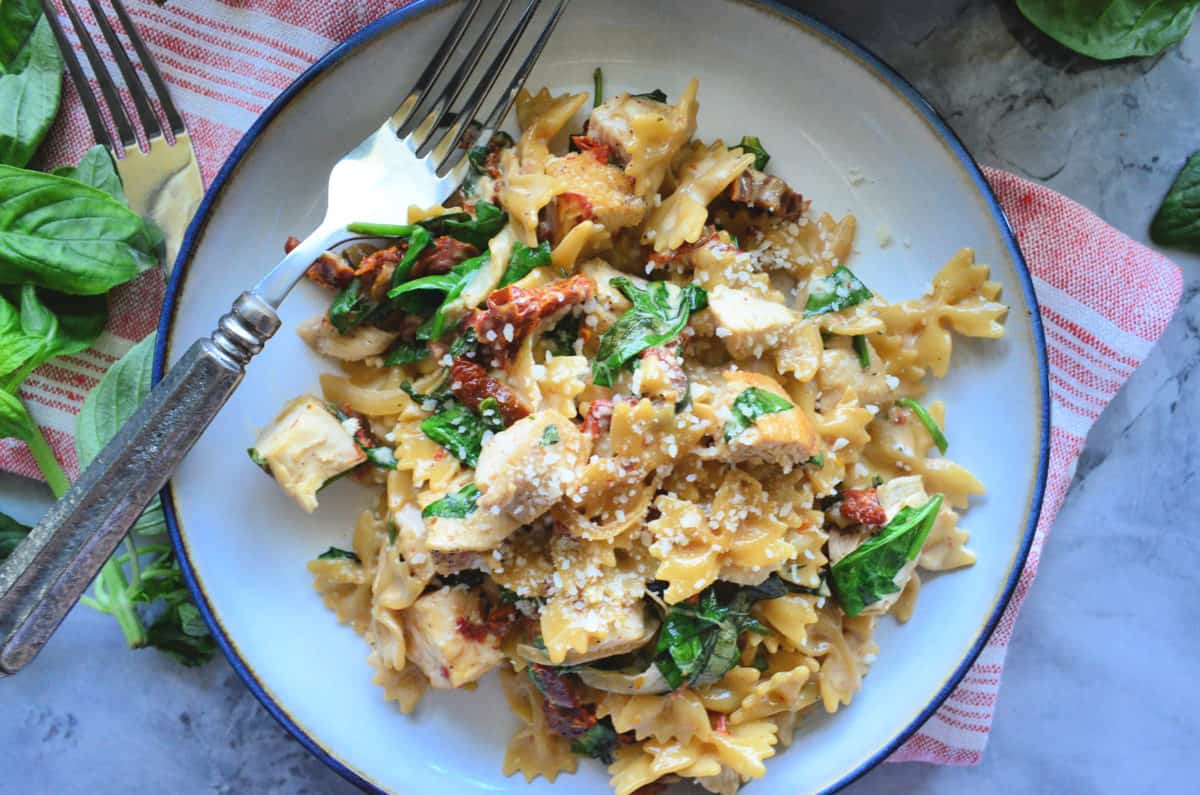 top view plated bowtie pasta, basil, sundried tomato chicken, and parmesan with fork.