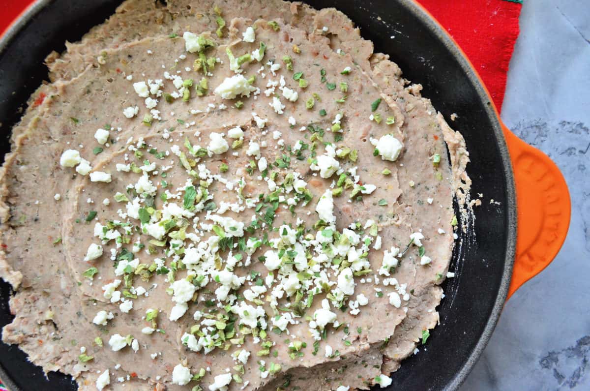Close up skillet filled with refried beans topped with chopped herbs and cheese.