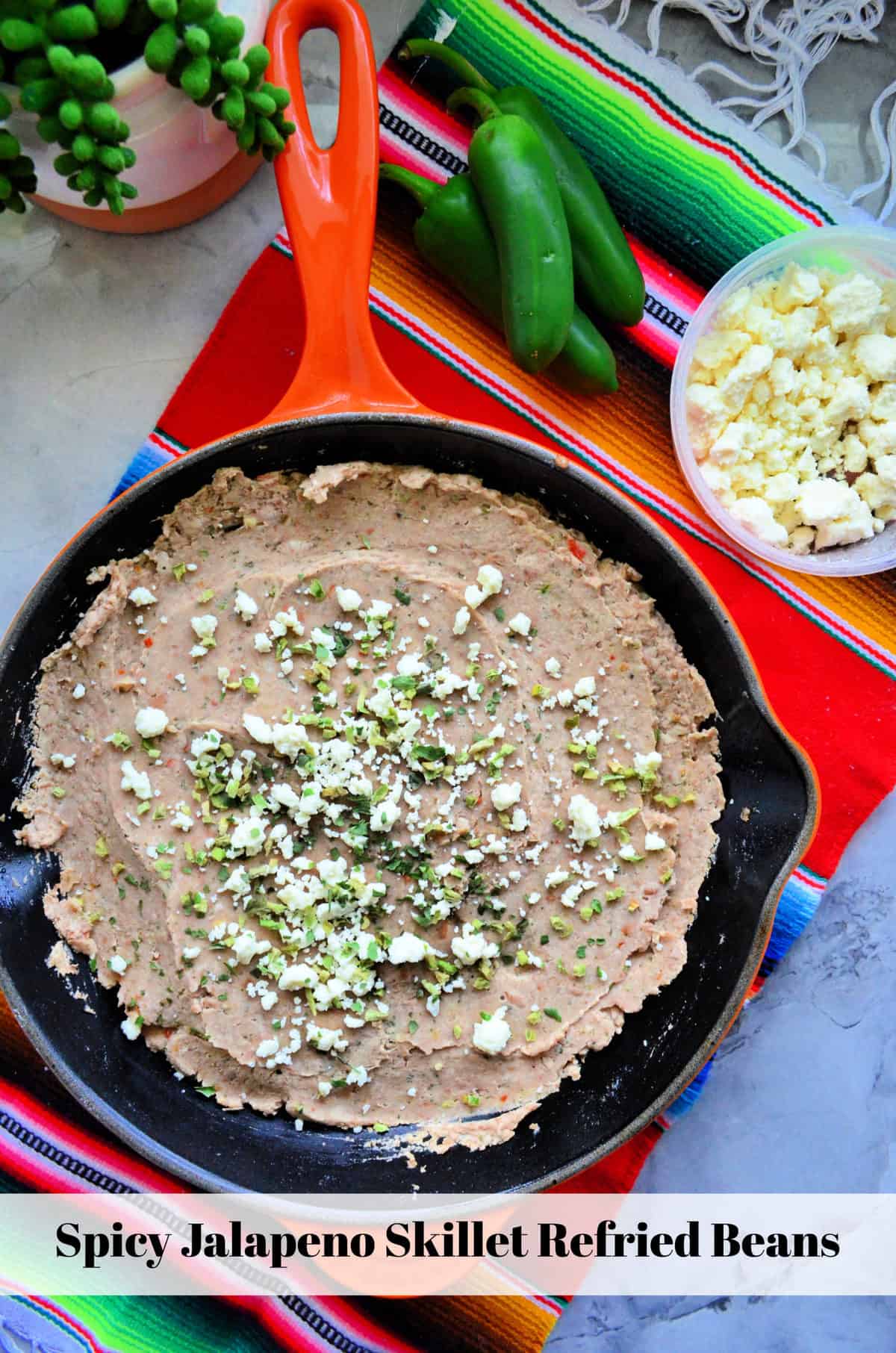 Skillet filled with refried beans topped with chopped herbs and cheese crumbles with title text.