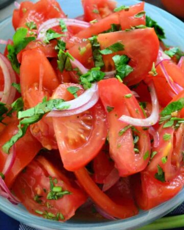 Blue bowl filled with tomatoes, red onions, and herbs.