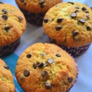 Closeup of 4 golden brown chocolate chip muffins on blue tableloth.