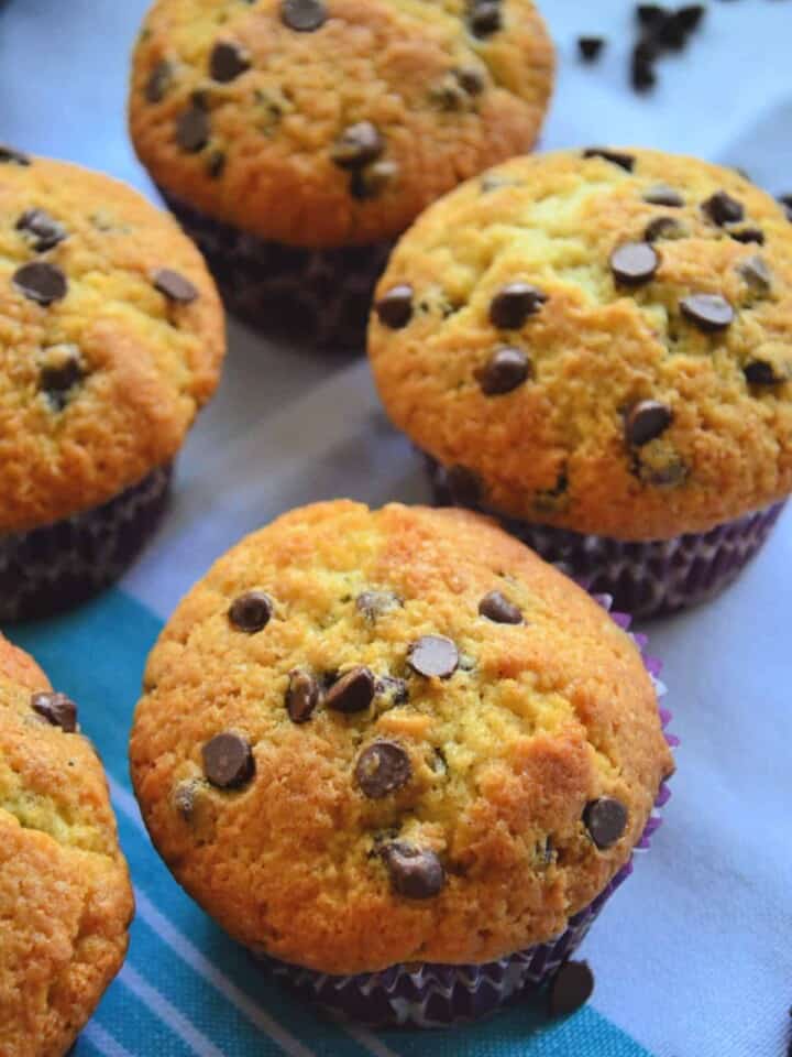 Closeup of 4 golden brown chocolate chip muffins on blue tableloth.