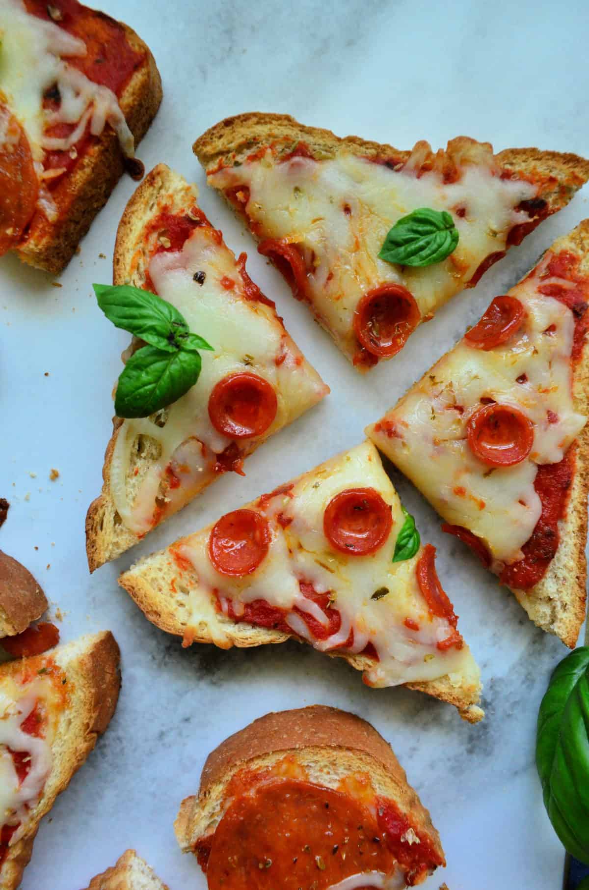 closeup piece of toast with marinara, pepperoni, and cheese, quartered on countertop.