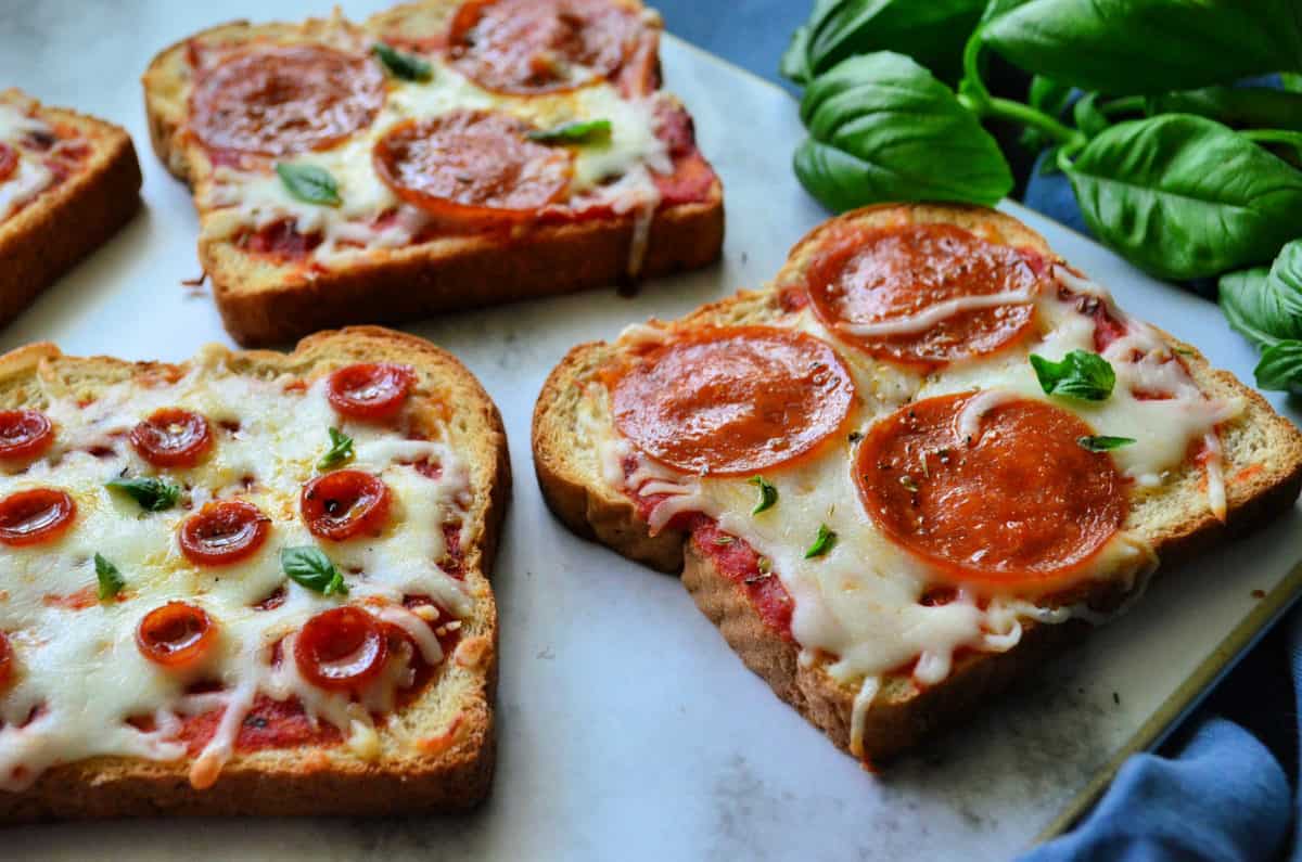 3pieces of toast with marinara, pepperoni, and cheese on countertop near basil.