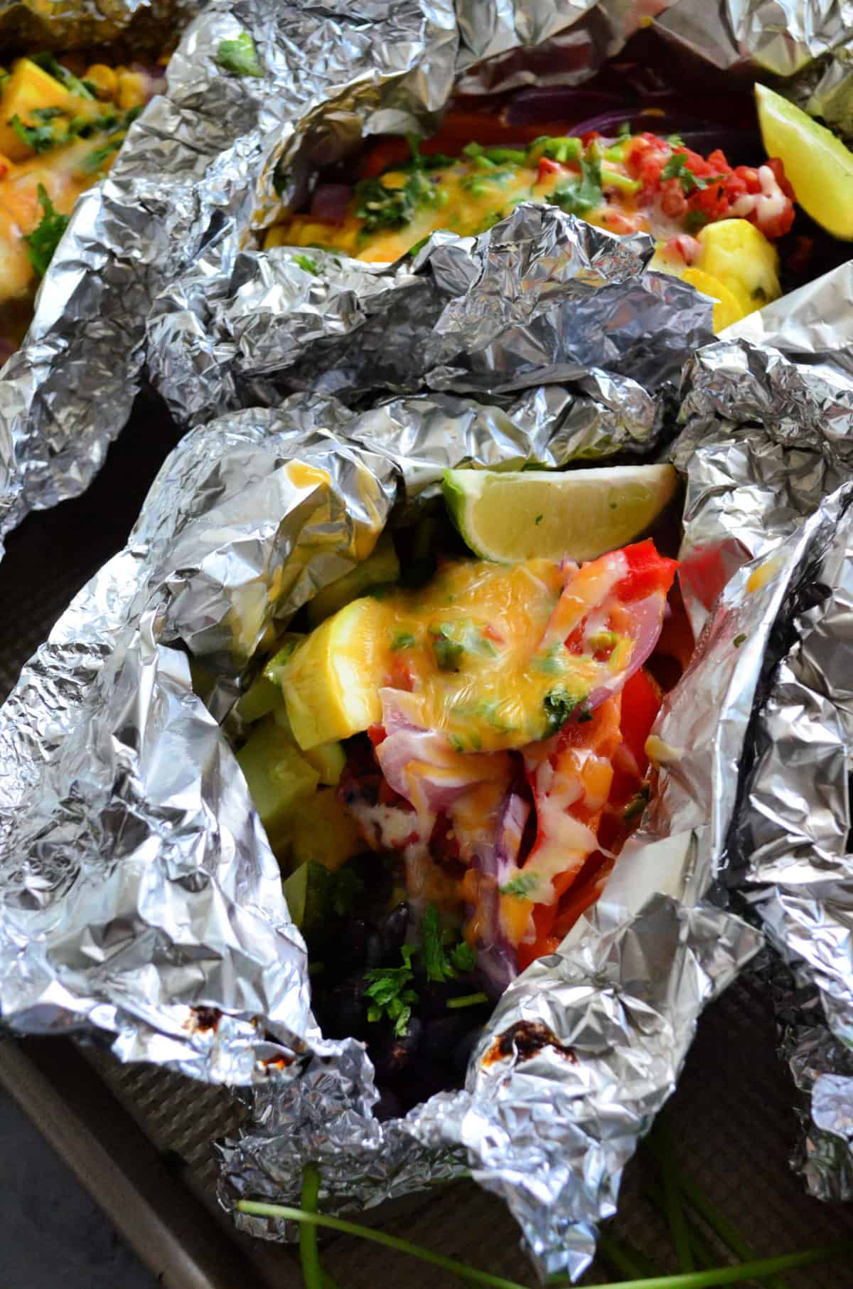 2 foil packets of melted cheese over veggies up close.