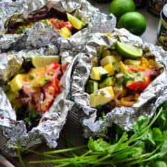 3 aluminum foil packets set next to cilantro bunch and opened to reveal veggies.