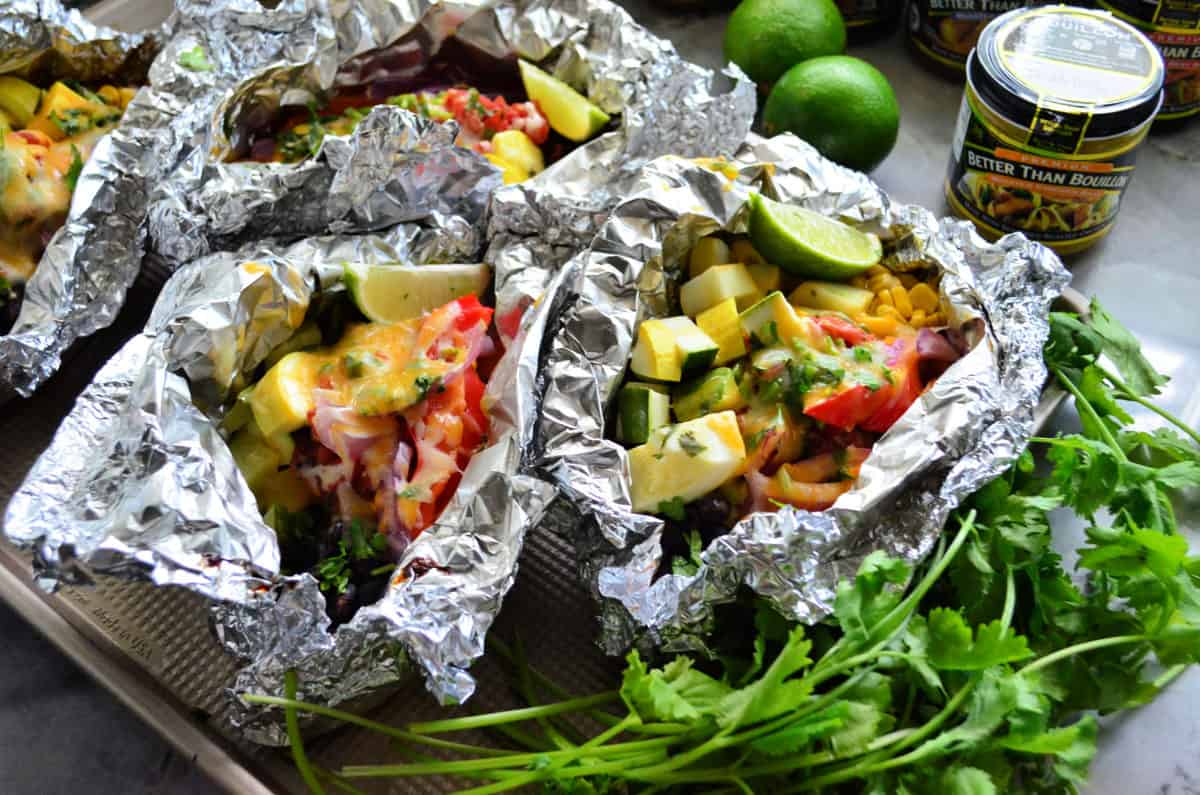 3 aluminum foil packets set next to cilantro bunch and opened to reveal veggies.