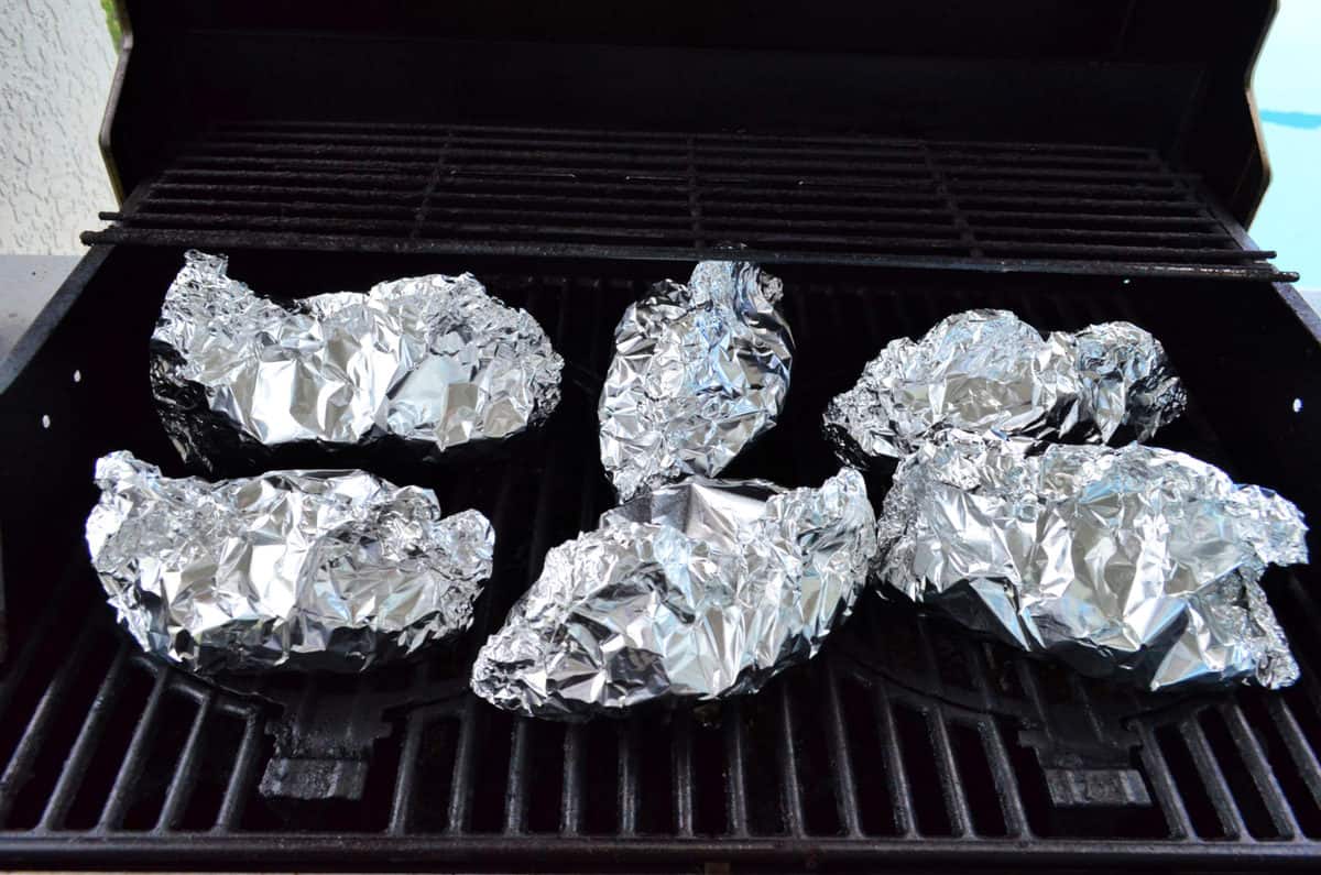 6 closed aluminum foil packets on open grill top.