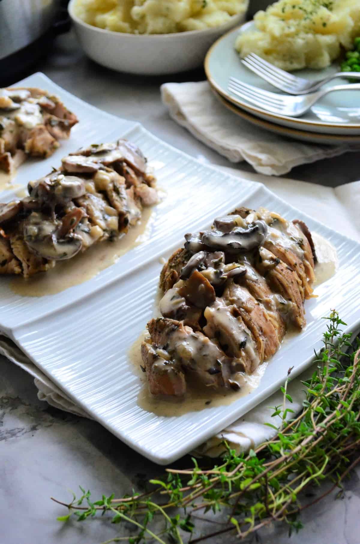 3 sliced turkey tenderloins plated with mushroom gravy with mashed potatoes in background.