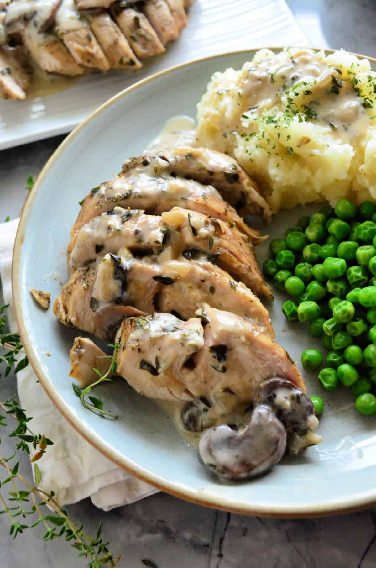 close up Sliced Turkey Tenderloin plated with mashed potatoes and peas drizzled with gravy.