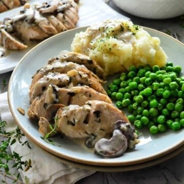 Plated turkey smothered in gravy and mushrooms with green peas and mashed potatoes.