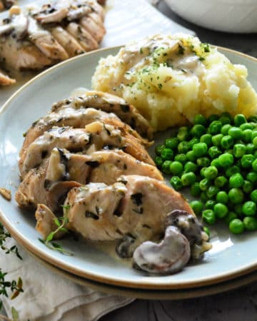 Plated turkey smothered in gravy and mushrooms with green peas and mashed potatoes.