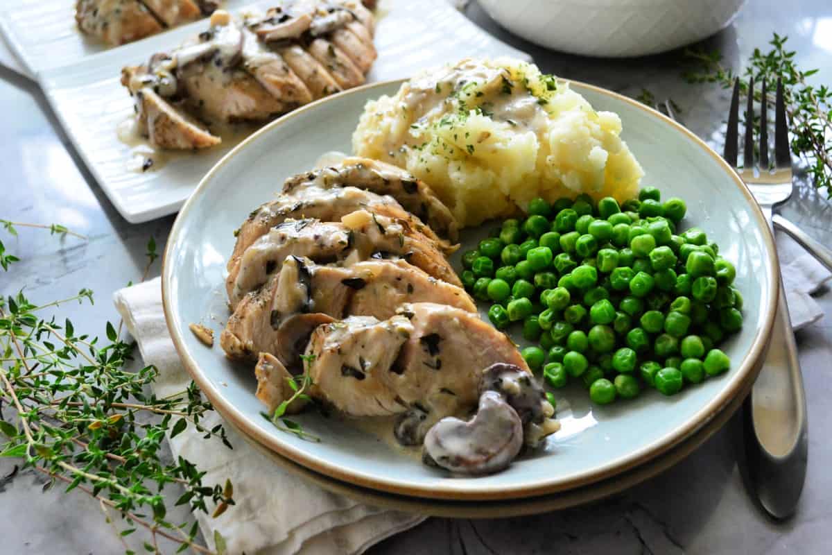 Plated turkey smothered in gravy and mushrooms with green peas and mashed potatoes.