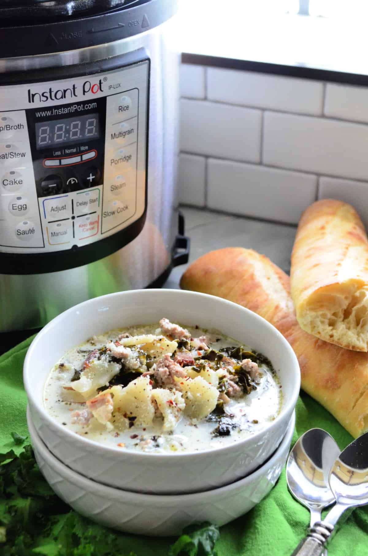 Bowl of creamy soup with potatoes and herbs on top in front of instant pot.